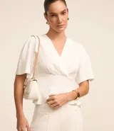 Blusa blanca de crepé con escote en V sobrepuesto, mangas cortas y recorte en la cintura con aspecto de volado.