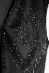 Chaleco corto negro con efecto ante, escote en V y cierre frontal con botones. Presenta apliques de abalorios brillantes con diseño floral.