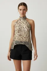 Top sin mangas de poliéster con estampado abstracto en tonos beige, marrón y dorado. Presenta cuello halter con abertura en la espalda y cierre con botones.
