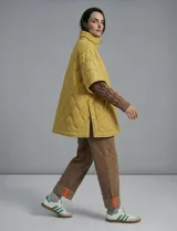 Poncho acolchado color mostaza con cuello alto y abertura frontal con cierre. Presenta un patrón capitoné de formas ovaladas y bolsillos delanteros.