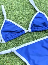 Bikini de dos piezas color azul eléctrico con ribete blanco. El corpiño es de estilo triángulo con tirantes finos regulables y la bombacha es colaless regulable con tiras laterales finas.
