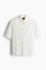 Camisa blanca de manga corta en tejido de algodón con textura. Modelo con cuello inglés, tapeta lisa, bolsillo superior abierto, canesú en la espalda y bajo recto. Corte estándar para una silueta clásica y cómoda.