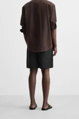 Bermuda regular fit negra confeccionada en tejido de lino. Cintura elástica ajustable con cordón y pliegues frontales. Bolsillos frontales y detalle de bolsillos traseros de plastrón.