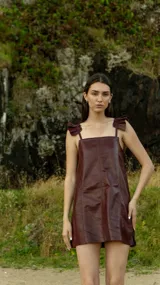 Vestido corto de cuero sintético color burdeos, con breteles finos regulables y volados en los hombros. Corte recto y largo a la altura del muslo.