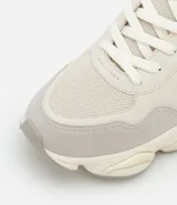 Championes dad sneaker grises con recortes en cuero sintético, cordones blancos y suela chunky de goma color crema.