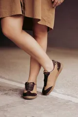 Zapatillas urbanas de cuero color beige con puntera y cordones marrones. Presentan un panel de animal print en el talón y suela de goma color caramelo.