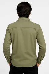 Camisa manga larga color verde militar, con cuello clásico, cierre frontal con botones a tono, dos bolsillos de parche con botón en el pecho y puños abotonados.