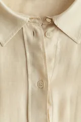 Camisa color crema de manga larga con puños abotonados, cuello clásico, cierre frontal con botones y bajo redondeado.