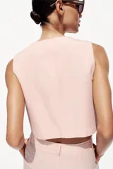 Chaleco color rosa pálido de cuello redondo y sisa. Bajo con aberturas delanteras y cierre frontal con botones.