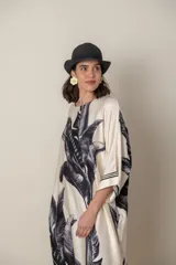 Vestido largo color natural con estampado de hojas de palmera en tonos verdes. Tiene corte amplio tipo túnica, cuello redondo, mangas tres cuartos, bolsillos laterales y ruedo con ribete.