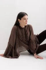 Camisa marrón de algodón con cuello mao, mangas largas abullonadas con puños elásticos y detalle de volados en el frente.