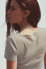 Camiseta color beige de tejido de punto, con cuello halter y escote pico. Tiene cierre frontal con botones y mangas cortas.
