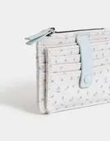 Billetera pequeña de cuerina estampada con flores de colores. Tiene cierre superior con tirador rosa, lazo con broche a presión y compartimentos para tarjetas.