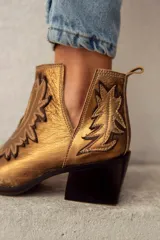 Botas cortas de cuero color bronce con bordados y recortes con motivos de estrellas.