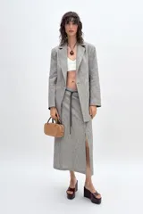 Falda midi de lino color gris con textura. Tiene tiro alto, cinturón fino del mismo tejido y abertura frontal. Cierre lateral con cremallera oculta.