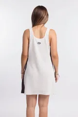 Vestido corto de punto waffle color crudo, con cuello redondo y sisas con ribete marrón. Presenta un logo bordado en el pecho y una banda lateral marrón.