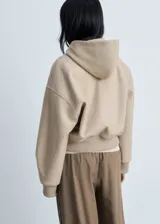 Chaqueta beige con capucha, cierre frontal con cremallera, puños y cintura elásticos.