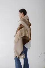 Ruana de lana con diseño abstracto en tonos beige, marrón y blanco. Presenta flecos en el borde inferior y capucha.