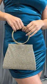 Cartera de mano tipo sobre, cubierta de brillos dorados, con manija circular metálica dorada.