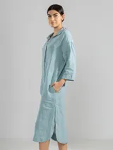 Camisa larga blanca de lino italiano, con cuello clásico, mangas 3/4, silueta fluida, dobladillo curvado en las costuras laterales y bolsillos discretos.