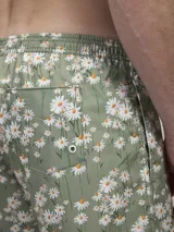 Short de baño verde con estampado de margaritas blancas y cordón ajustable naranja.