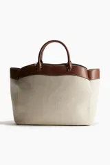 Bolso shopper de lona color beige con detalles en cuero marrón. Tiene doble asa de mano y compartimento interno con cierre.