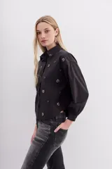 Camisa negra holgada de corte clásico, con cuello camisero, mangas largas con puños y bordados de piedras.