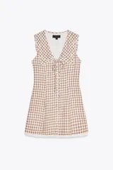 Vestido corto de escote pico con cuello bobo y manga sisa. Detalle de flores bordadas y entredoses. Forro interior. Cierre frontal con botones forrados y lazada. Estampado a cuadros vichy color marrón y blanco.