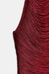 Vestido corto color rojo oscuro, con cuello halter ajustable con lazos y cuerpo cubierto de flecos horizontales que crean un efecto de cascada.