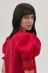Blusa roja de algodón con mangas cortas abullonadas y puños con detalle de bordado en color amarillo/naranja.