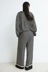 Pantalón de tiro alto con elástico en la parte posterior de la cintura y cierre oculto lateral. Presenta bolsillos discretos en las costuras laterales y piernas anchas con pliegues adelante y atrás. Diseño estampado con motivos geométricos en blanco y negro.