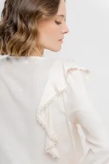 Blusa color crema con volados en el frente, detalle de puntilla y bordados florales en mangas.