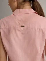 Camisa blanca sin mangas, con cuello camisero, cierre frontal con botones de madera y bolsillo de parche en el pecho.
