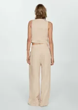 Pantalón de vestir color beige, de corte wide leg, tiro medio, con pinzas delanteras y cierre frontal con botón, gancho y cremallera.