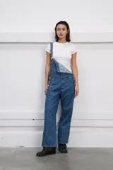 Jardinero denim azul con bolsillo en la pechera, botones metálicos y corte amplio de pierna recta.