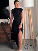 Vestido largo negro, sin mangas, con cuello drapeado y detalle de nudo fruncido con hebilla metálica en la cintura. Presenta una abertura alta en la falda.