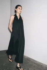 Vestido midi negro de lino, con cuello halter, hombros descubiertos, espalda descubierta, cierre frontal con botones y bajo asimétrico.