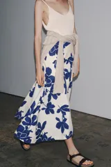 Falda midi de tiro medio confeccionada en hilatura de algodón, color blanco con estampado de flores azules. Cierre lateral con botones.