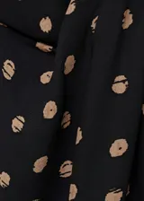 Blusa negra con estampado de lunares color beige, de manga corta y cuello alto con detalle drapeado.