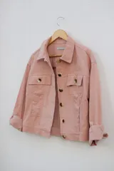 Campera de pana color rosa con botones dorados, cuello clásico y bolsillos con solapa en el pecho.