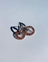 Par de aros colgantes con argollas doradas y dijes circulares de resina transparente con incrustaciones de strass de colores. El dije mide aproximadamente 1.5cm de diámetro.