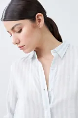 Camisa oversize celeste y blanca a rayas verticales, con cuello mao y mangas largas con puños abotonados.
