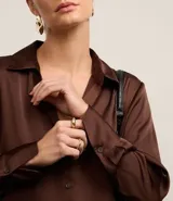 Camisa blanca de satén con cuello inglés, manga larga y cierre frontal con botones.