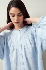 Camisa celeste a rayas verticales, de corte amplio y mangas 3/4. Presenta cuello mao, cierre frontal con botones irregulares y detalle de pespuntes y pinzas en el canesú.
