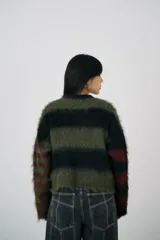 Sweater tejido de punto con rayas horizontales en tonos verde oliva, negro y rojo. Diseño suave y esponjoso, con corte boxy y hombros caídos.