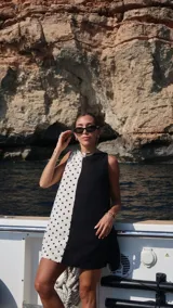Vestido corto sin mangas, con escote recto y corte a la rodilla. Presenta un diseño bicolor, con un lado blanco con lunares negros y otro lado negro liso.