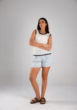 Blusa blanca de tejido calado, sin mangas y con cuello redondo ribeteado en negro.