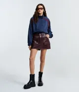 Short pollera corto color bordó, confeccionado en poliuretano (PU), con bolsillos delanteros grandes con solapas y cierre por cremallera.