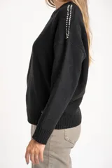 Sweater de punto negro, corte oversize, con cuello redondo y apliques de tachas plateadas en los hombros.