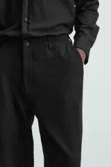 Pantalón negro de corte regular fit, con bolsillos laterales y bolsillos traseros de vivo. Presenta un bajo con vuelta y cierre frontal con cremallera y botón.